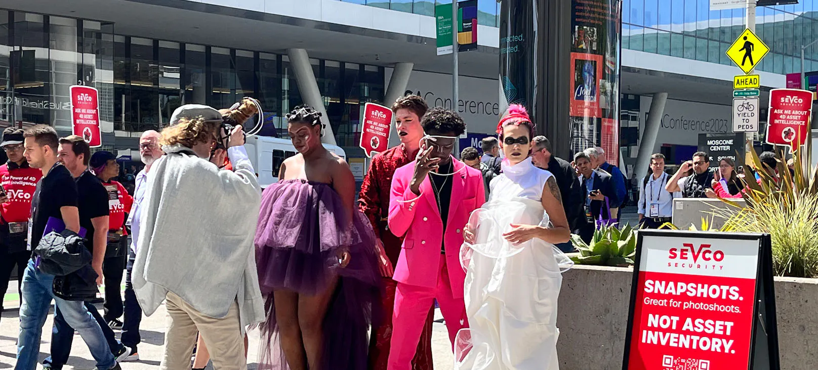 Sevco Security’s 4D Asset Intelligence guerrilla marketing activation at RSAC, featuring brightly dressed performers posing for photos outside Moscone Center alongside branded cybersecurity messaging about asset visibility.