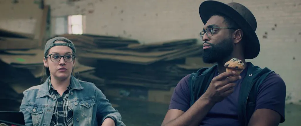 Vertex11 Hacker Status Meeting cybersecurity video campaign featuring two hackers in a warehouse, one holding a muffin, in a humorous role-reversal concept that exposes common cybersecurity defense gaps.